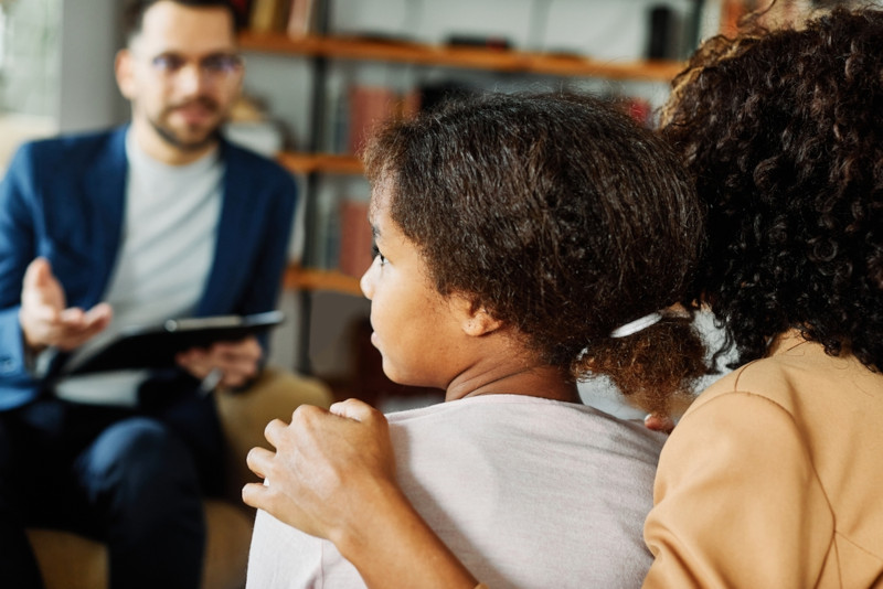 A child looking off to the side as her mother speaks with a family social worker