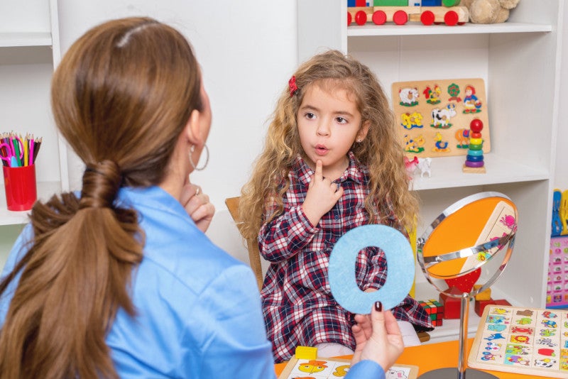 A young girl getting speech therapy from an SLP