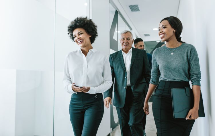 Smiling businesspeople walk down an office corridor.