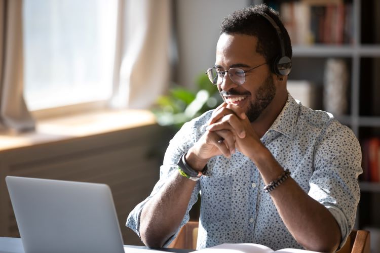An online student wearing headphones laughs while participating in a remote classroom via laptop.